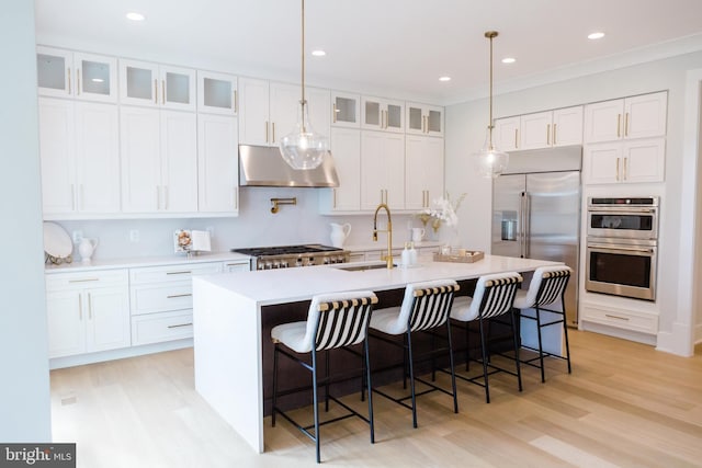 kitchen with a center island with sink, light hardwood / wood-style flooring, appliances with stainless steel finishes, a breakfast bar area, and white cabinets