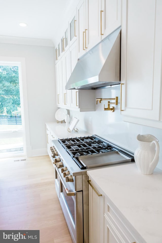 kitchen with light stone countertops, high end white range, white cabinetry, light hardwood / wood-style flooring, and crown molding