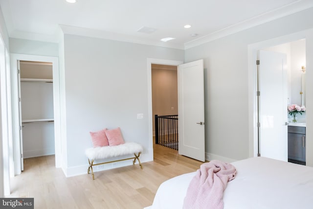 bedroom with a spacious closet, crown molding, light hardwood / wood-style floors, and ensuite bath