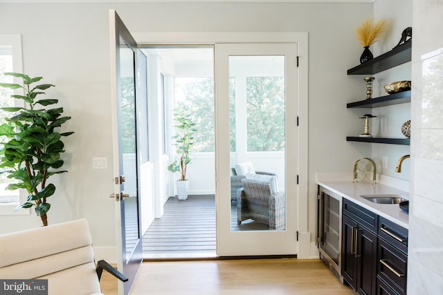 doorway to outside featuring light wood-type flooring, sink, and beverage cooler