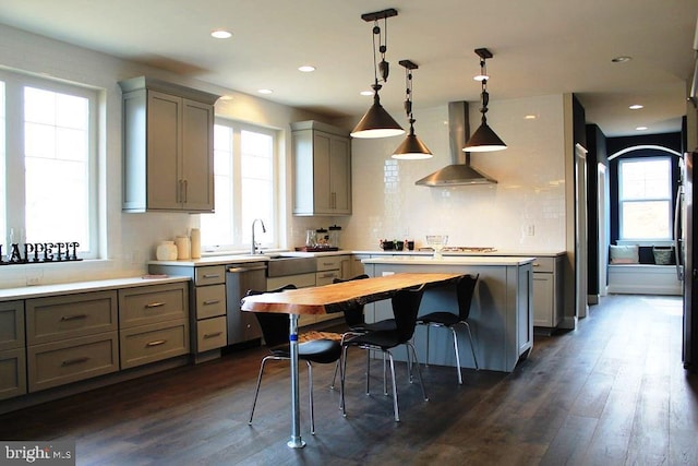 kitchen with stainless steel dishwasher, sink, wall chimney range hood, decorative light fixtures, and dark hardwood / wood-style floors