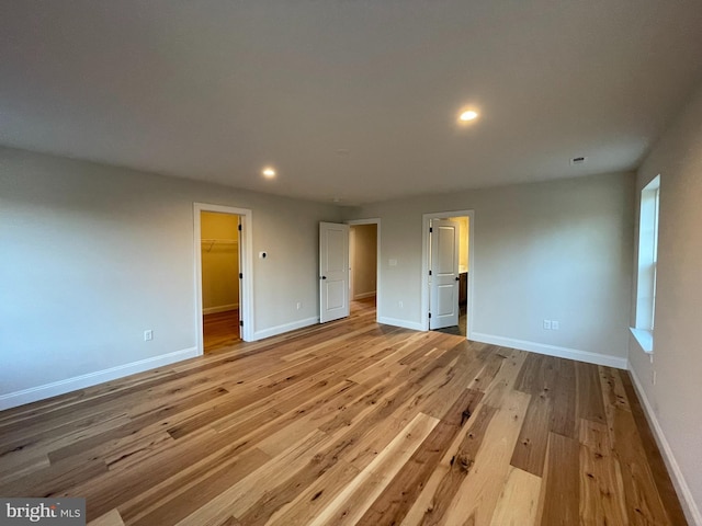 unfurnished bedroom with a walk in closet, a closet, and light hardwood / wood-style floors