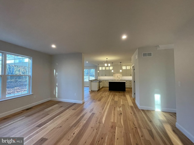 unfurnished living room with light wood-type flooring, sink, and a chandelier