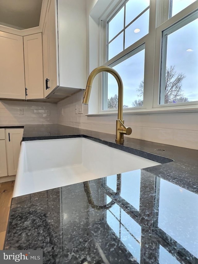 room details with tasteful backsplash, dark stone countertops, sink, and white cabinets