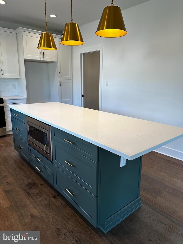 kitchen with decorative backsplash, stainless steel appliances, dark wood-type flooring, white cabinetry, and hanging light fixtures