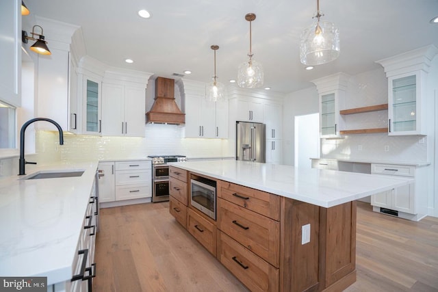 kitchen featuring custom range hood, stainless steel appliances, sink, white cabinets, and a center island