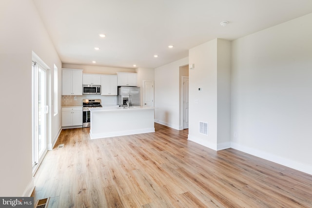 kitchen featuring an island with sink, light hardwood / wood-style flooring, white cabinets, and stainless steel appliances