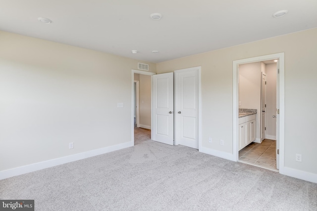 unfurnished bedroom featuring ensuite bathroom and light carpet