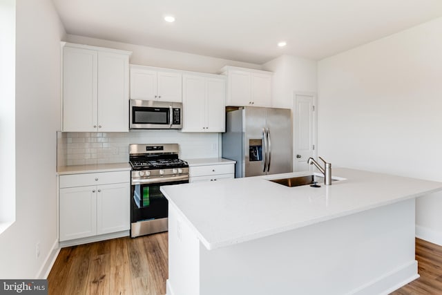 kitchen featuring light wood-type flooring, stainless steel appliances, white cabinetry, and a kitchen island with sink