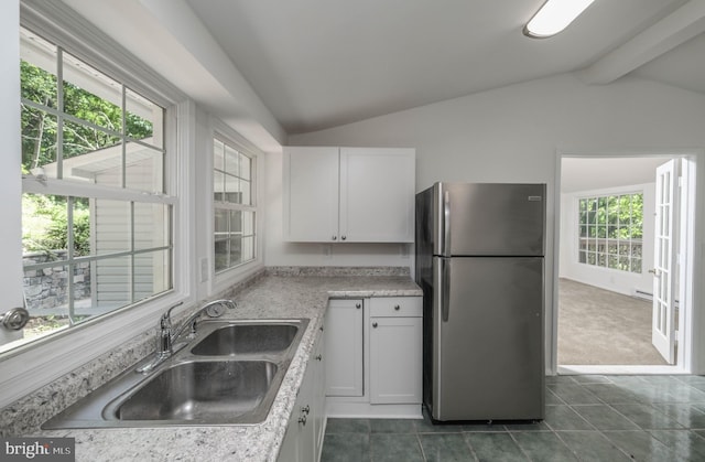 kitchen featuring sink, dark tile patterned flooring, white cabinets, vaulted ceiling with beams, and stainless steel refrigerator