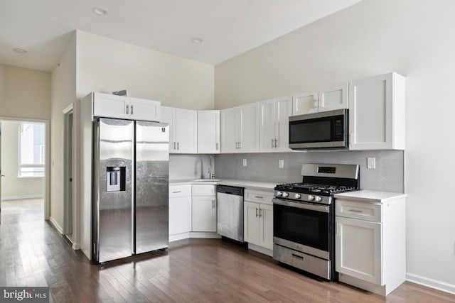 kitchen featuring backsplash, a high ceiling, appliances with stainless steel finishes, dark hardwood / wood-style flooring, and white cabinetry