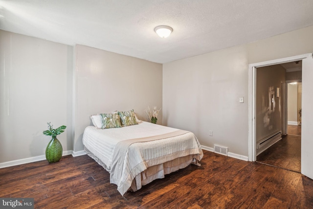 bedroom featuring a textured ceiling, dark hardwood / wood-style floors, and a baseboard heating unit