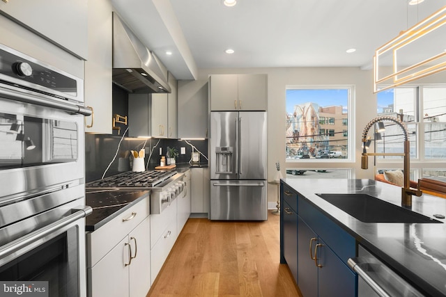 kitchen with appliances with stainless steel finishes, wall chimney exhaust hood, blue cabinetry, light hardwood / wood-style floors, and white cabinetry