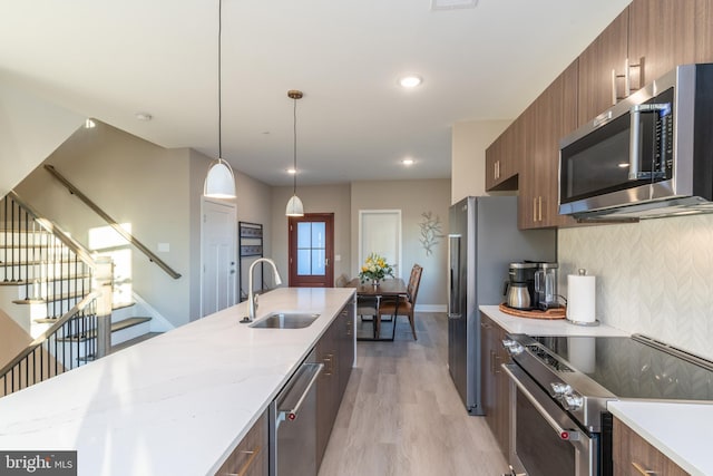 kitchen with backsplash, appliances with stainless steel finishes, light hardwood / wood-style floors, sink, and pendant lighting