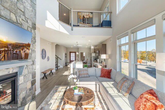 living room featuring a towering ceiling, wood-type flooring, and a stone fireplace