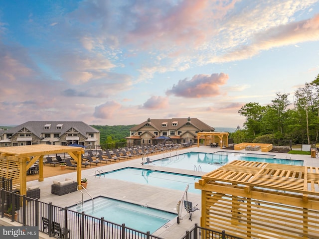 pool at dusk with a patio, a pergola, a jacuzzi, and a community pool