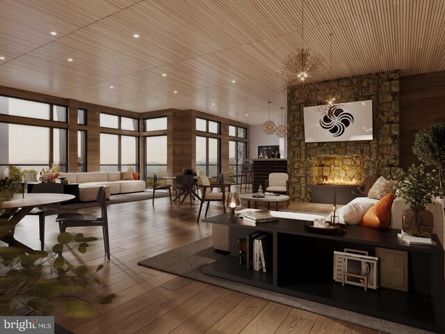 living room with wood-type flooring, plenty of natural light, an inviting chandelier, and a stone fireplace