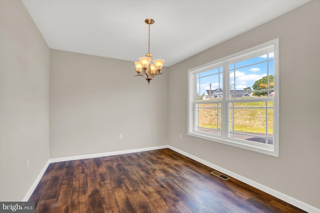 empty room featuring a healthy amount of sunlight, dark hardwood / wood-style floors, and a notable chandelier