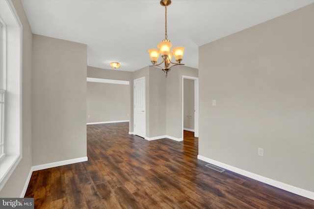 empty room featuring dark wood-type flooring and a notable chandelier