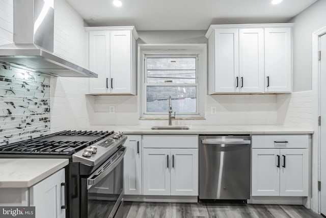kitchen featuring sink, wall chimney range hood, appliances with stainless steel finishes, white cabinets, and hardwood / wood-style flooring