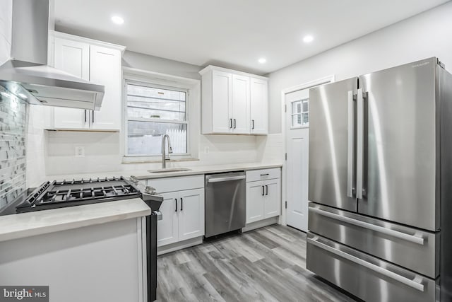 kitchen with white cabinets, wall chimney range hood, sink, light wood-type flooring, and stainless steel appliances