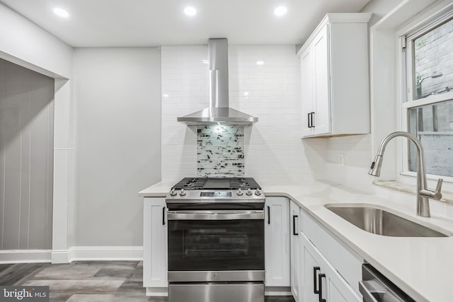 kitchen with light wood-type flooring, stainless steel appliances, sink, wall chimney range hood, and white cabinetry