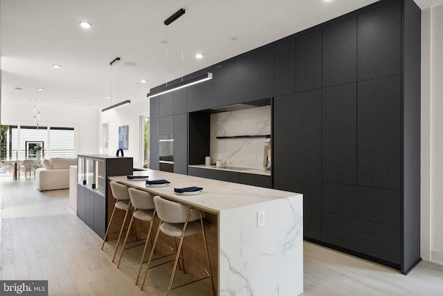 kitchen with light stone counters, a spacious island, hanging light fixtures, and light hardwood / wood-style flooring