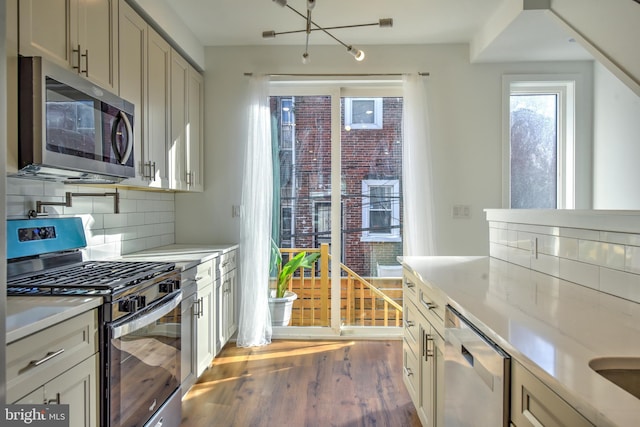 kitchen with appliances with stainless steel finishes, wood-type flooring, tasteful backsplash, a chandelier, and light stone counters