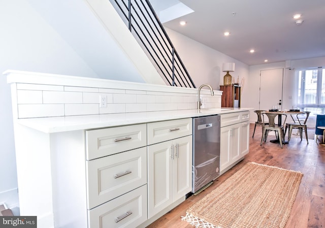 kitchen with backsplash, light hardwood / wood-style floors, stainless steel dishwasher, sink, and white cabinets