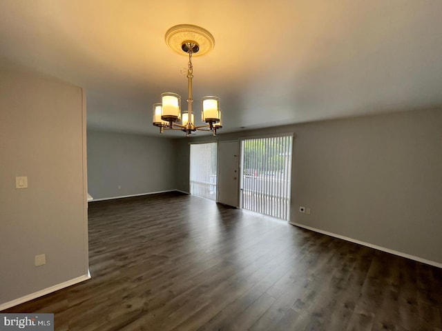 empty room featuring dark wood-type flooring and an inviting chandelier