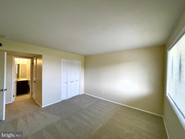 unfurnished bedroom featuring light colored carpet, ensuite bath, and a closet