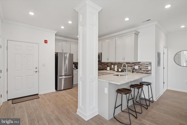 kitchen with ornate columns, stainless steel appliances, sink, light hardwood / wood-style flooring, and white cabinetry