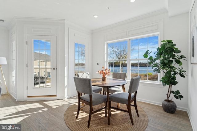 dining area featuring crown molding, plenty of natural light, a water view, and light wood-type flooring