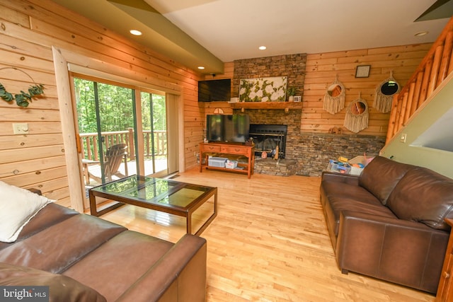 living room with a stone fireplace, wood walls, and light wood-type flooring