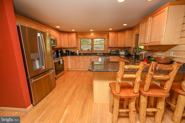 kitchen featuring kitchen peninsula, dark stone counters, a breakfast bar, stainless steel appliances, and light hardwood / wood-style floors