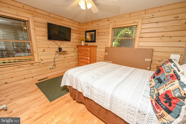 bedroom with ceiling fan, wooden walls, and wood-type flooring