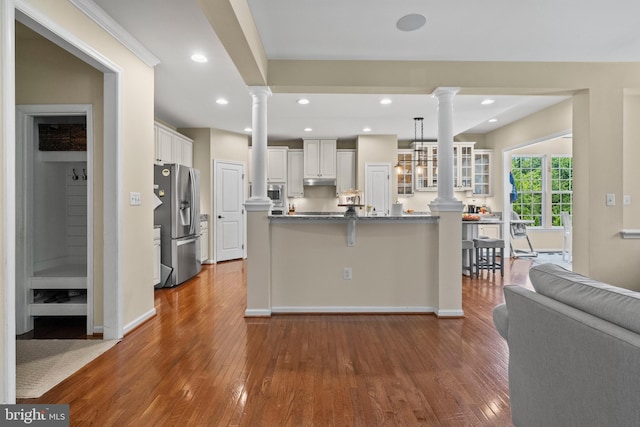 kitchen with a kitchen breakfast bar, hardwood / wood-style flooring, decorative light fixtures, white cabinetry, and stainless steel appliances