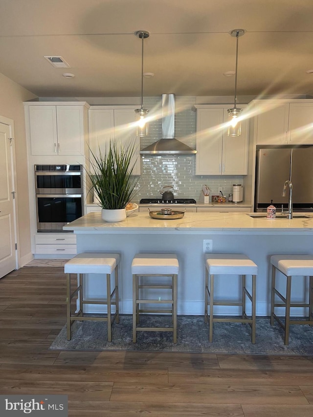 kitchen with pendant lighting, wall chimney exhaust hood, dark hardwood / wood-style floors, and a kitchen bar