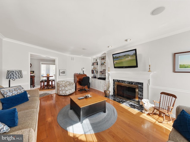 living room featuring a premium fireplace, ornamental molding, built in shelves, and wood-type flooring