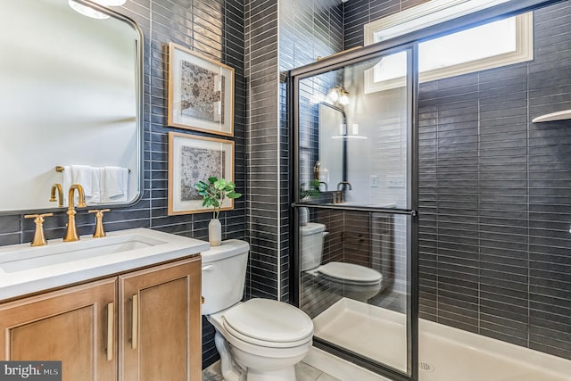 bathroom with vanity, a shower with door, tile patterned floors, toilet, and tile walls