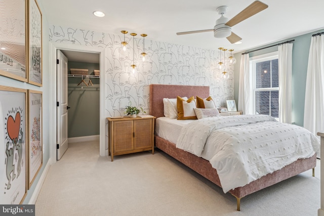 bedroom featuring a walk in closet, light carpet, a closet, and ceiling fan