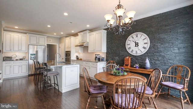 kitchen with appliances with stainless steel finishes, light stone counters, a kitchen island with sink, dark wood-type flooring, and hanging light fixtures