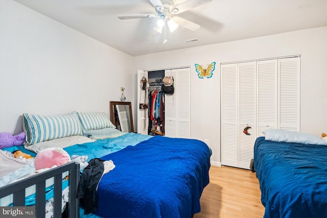 bedroom featuring wood finished floors, two closets, visible vents, and a ceiling fan