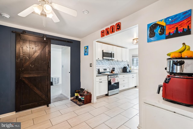 kitchen with white cabinets, a barn door, stainless steel appliances, and backsplash