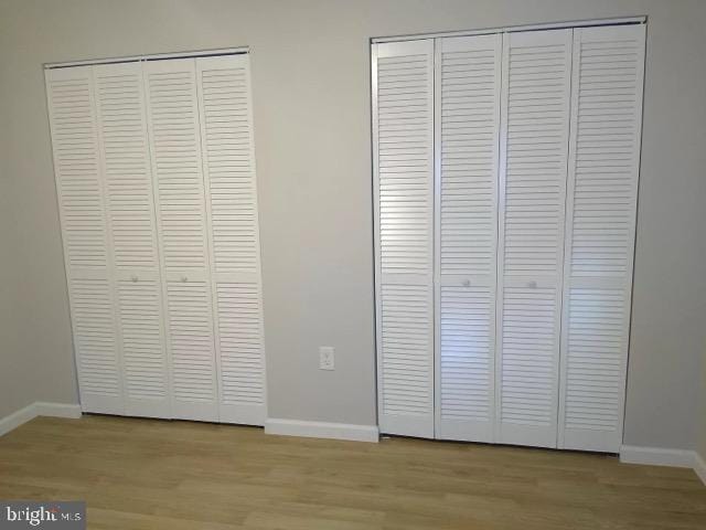 unfurnished bedroom with light wood-style floors, baseboards, and two closets