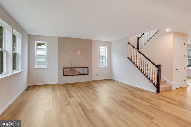 unfurnished living room featuring plenty of natural light, a tile fireplace, and light hardwood / wood-style flooring