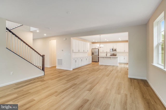 unfurnished living room with sink, light hardwood / wood-style flooring, and a notable chandelier