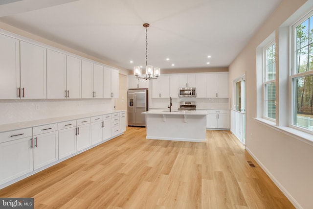 kitchen featuring light hardwood / wood-style flooring, white cabinets, stainless steel appliances, and decorative light fixtures