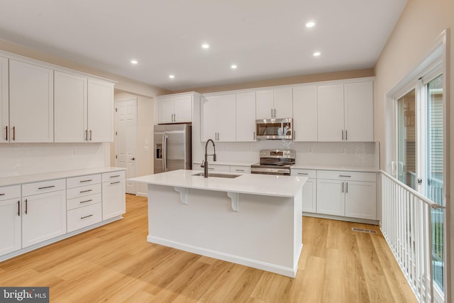 kitchen with appliances with stainless steel finishes, a kitchen island with sink, sink, light hardwood / wood-style flooring, and white cabinetry