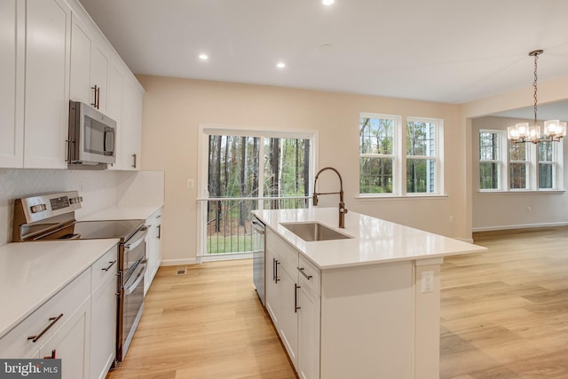 kitchen with appliances with stainless steel finishes, sink, pendant lighting, light hardwood / wood-style flooring, and an island with sink